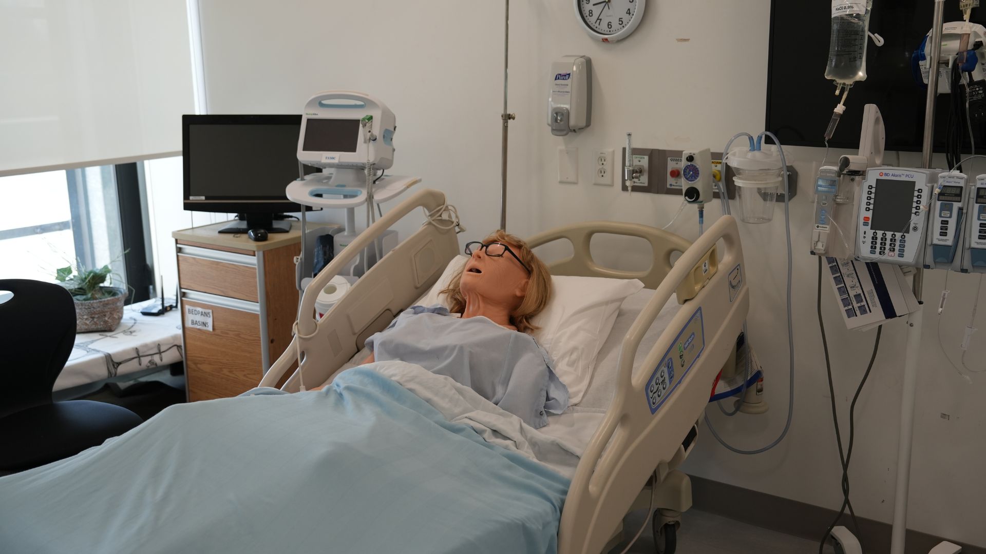 A nursing simulation mannequin in a hospital bed.