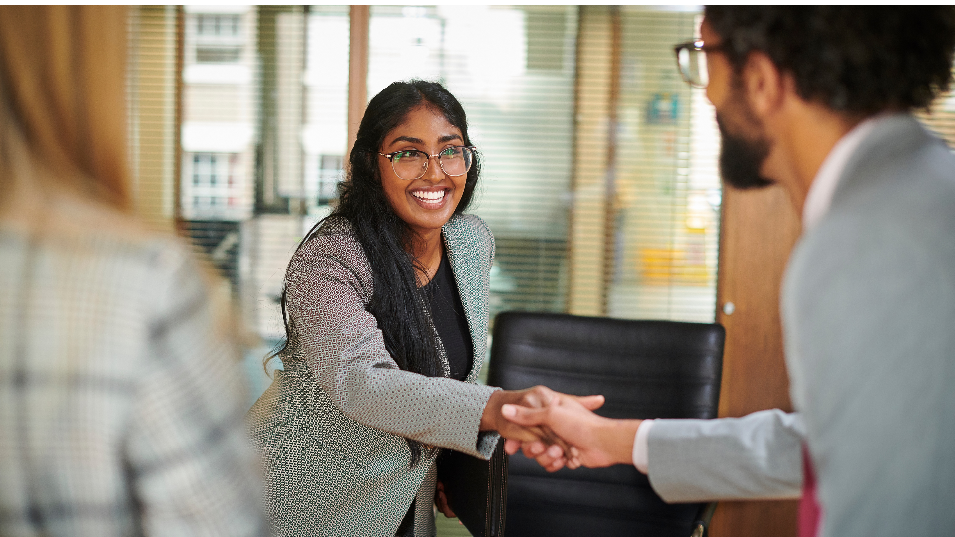 A woman leans across a table to shake hands with a male.
