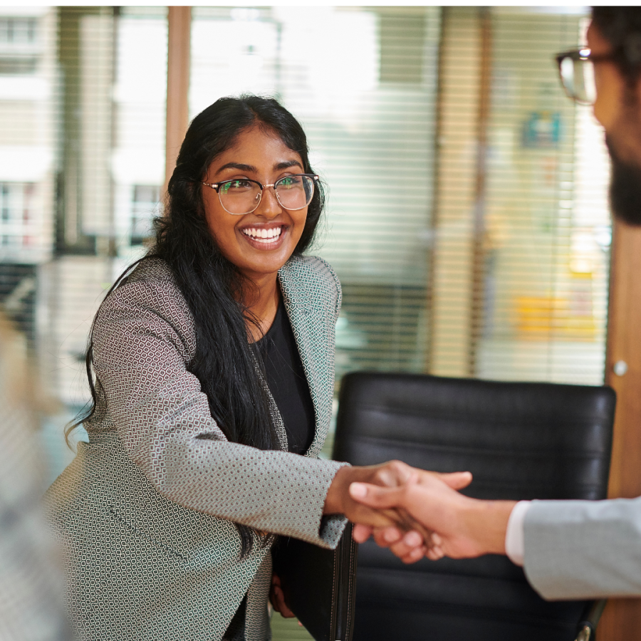 A woman leans across a table to shake hands with a male.