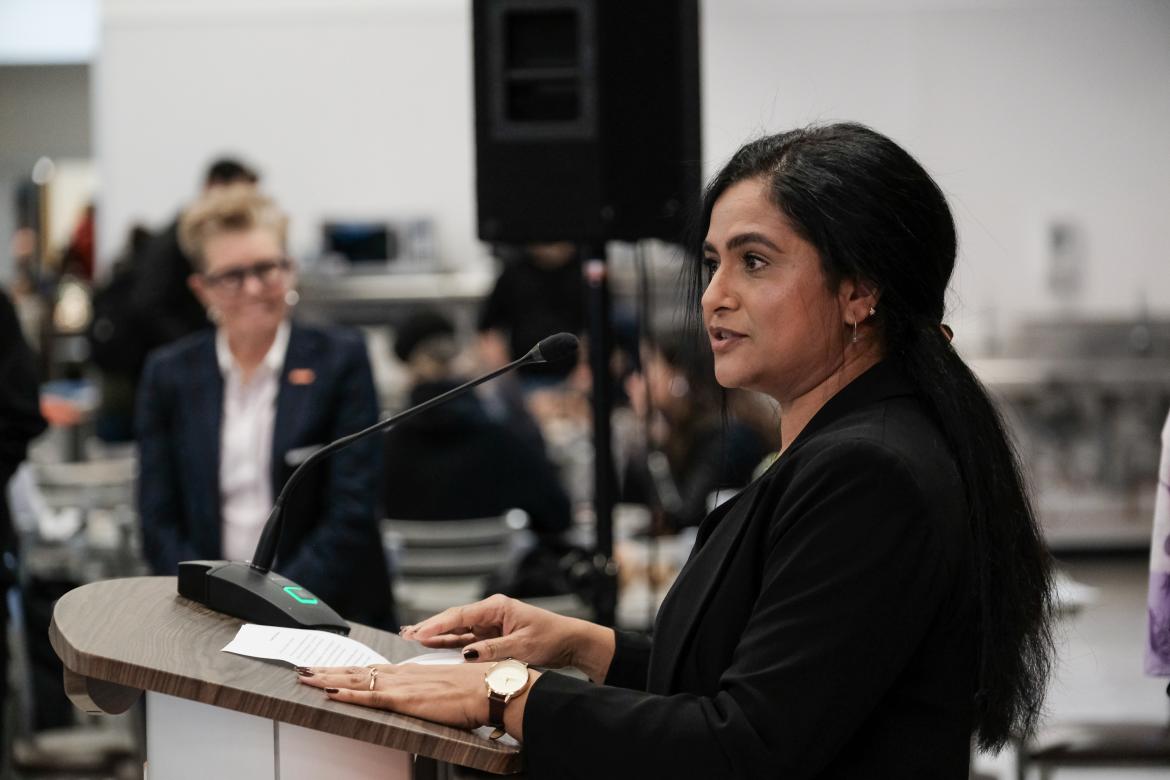 A dark-haired woman gives a speech at a podium while Langara President and CEO Dr. Paula Burns looks on.