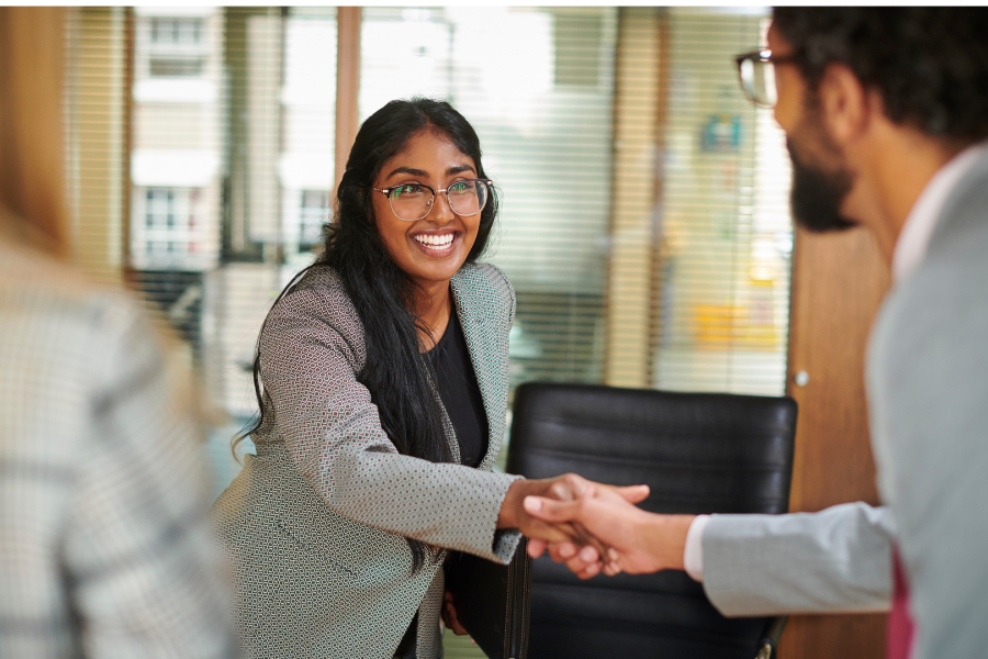 A woman leans across a table to shake hands with a male.