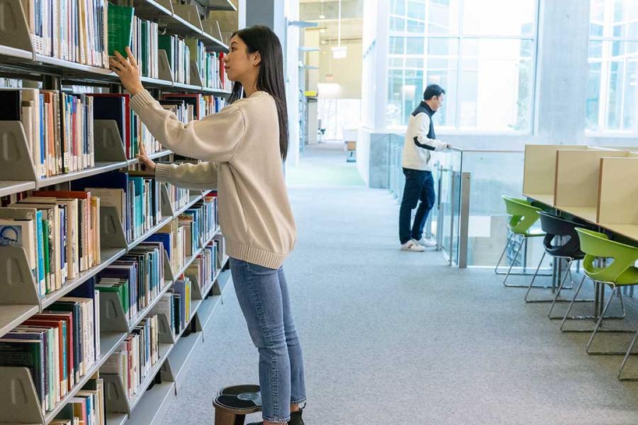 On the third floor of the library, a determined student is on a quest, her eyes scanning the shelves for the perfect book to complete her final assignment.