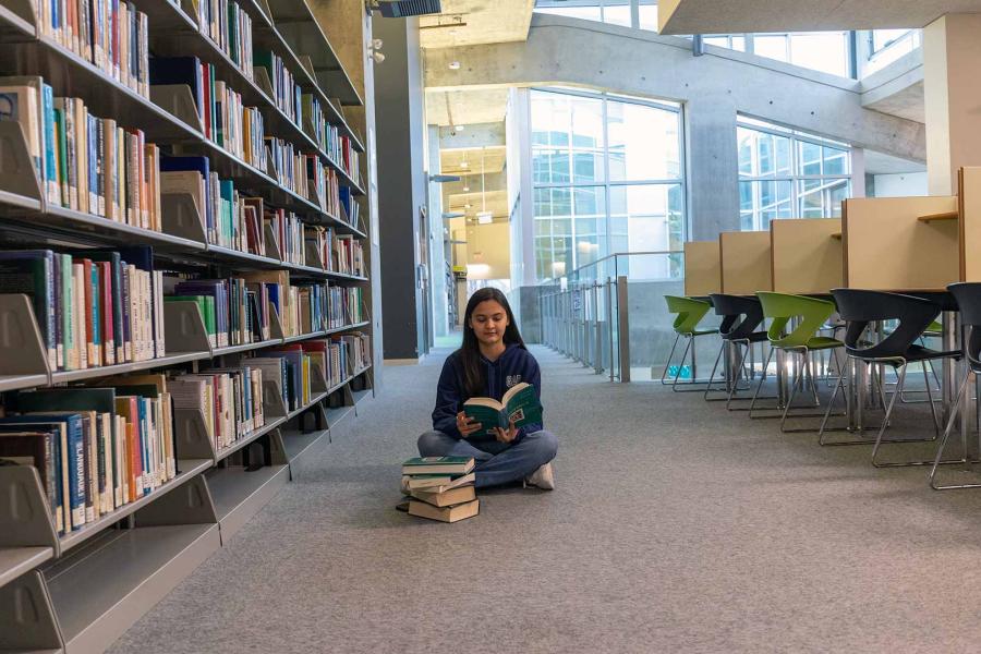 A dedicated student is actively exploring the shelves of the library, carefully selecting books to enhance their knowledge and fuel their academic pursuits.
