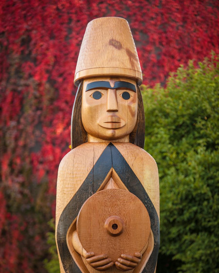 The Musqueam house post on campus wears a blanket and holds a spindle whorl